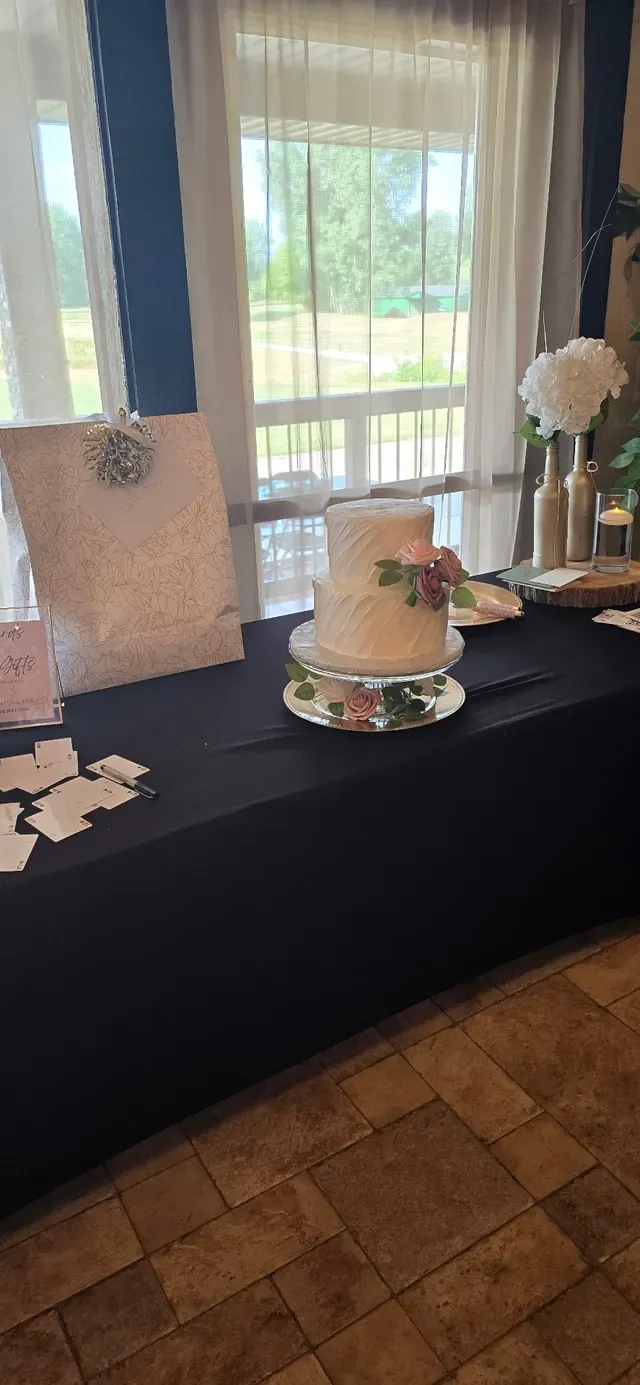 A tiered wedding cake on a black-clothed table beside scattered place cards