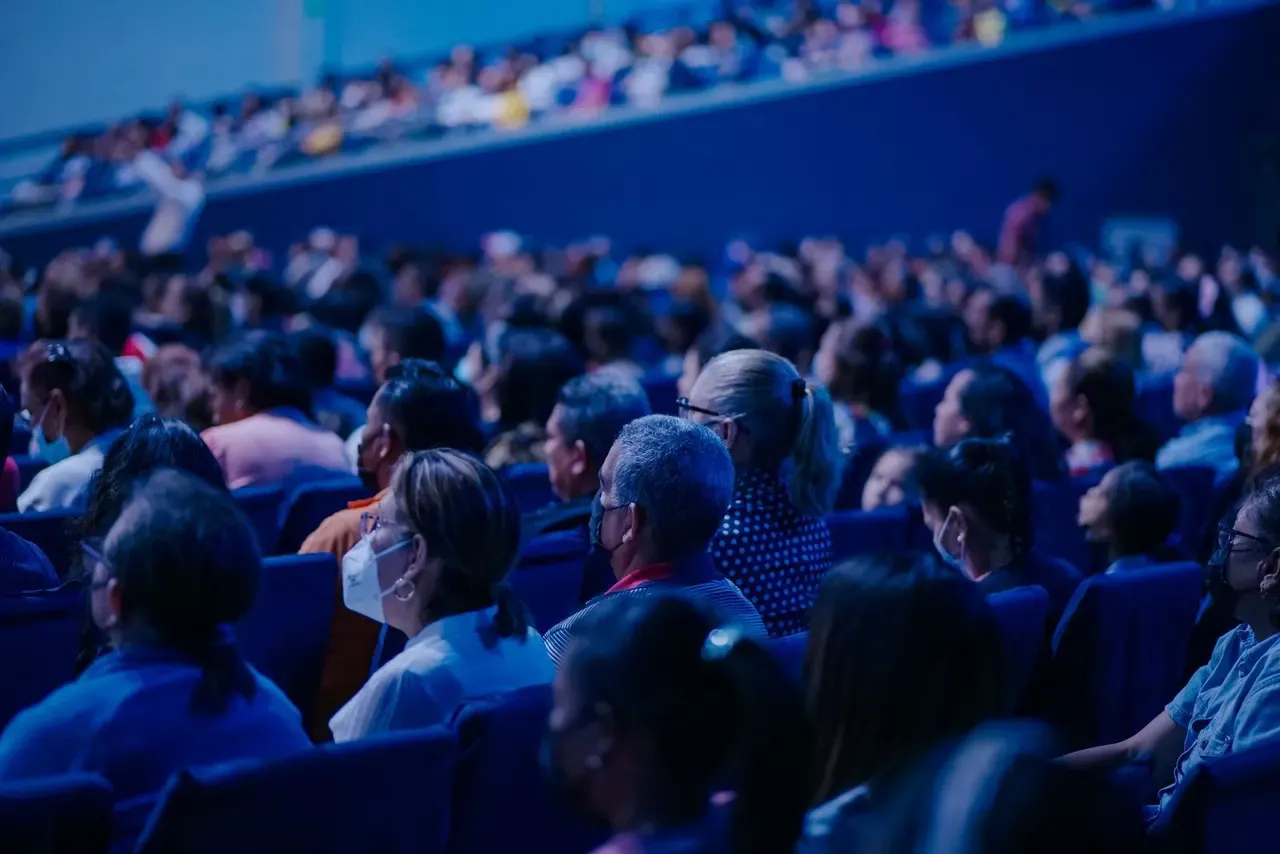 Rows of seated delegates seen from behind under blue stage lighting