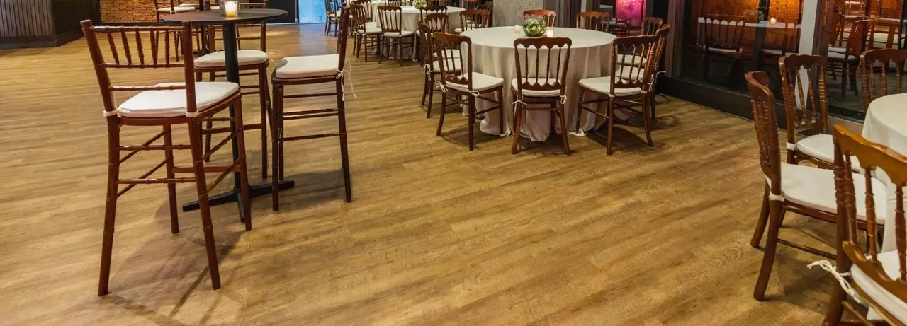 Round tables and chairs set out for a company dinner in a wood-floored hall