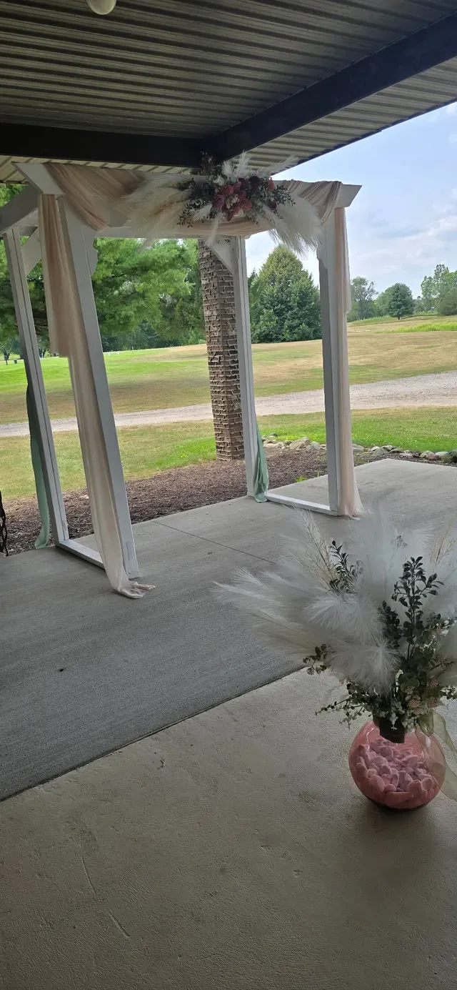 An empty covered patio decorated with pampas grass, looking out over a golf course