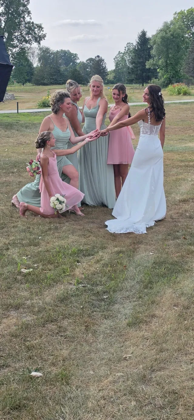 A flower girl straightening the back of a bride’s dress on a lawn