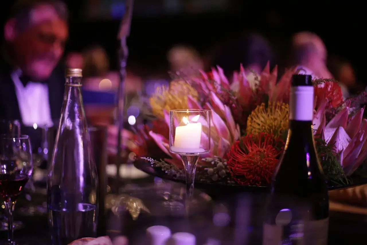 A candle burning beside flowers on a dark dinner table