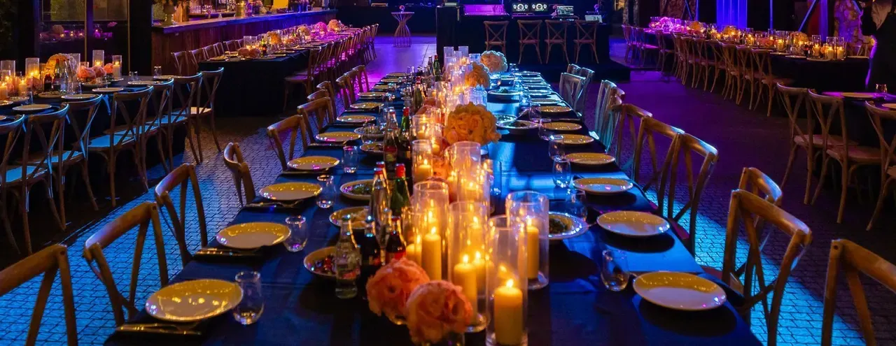 Long banquet tables laid with candles under a marquee lit purple and gold