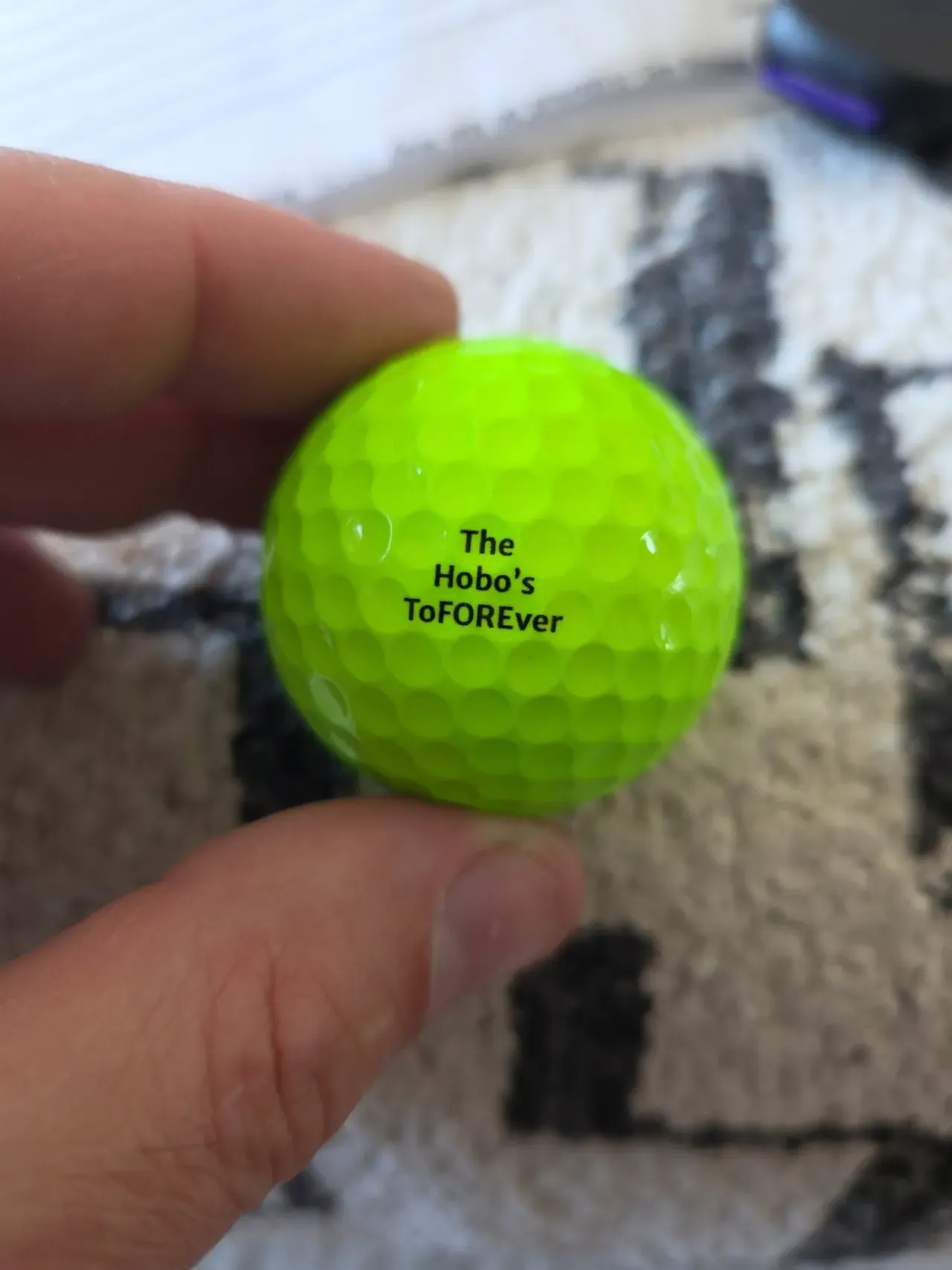 A green golf ball printed with a wedding favour message, held between finger and thumb