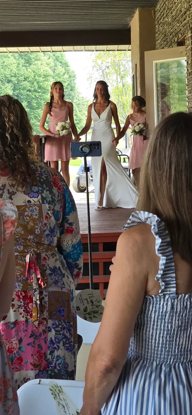 A phone on a small tripod filming a wedding ceremony while guests watch