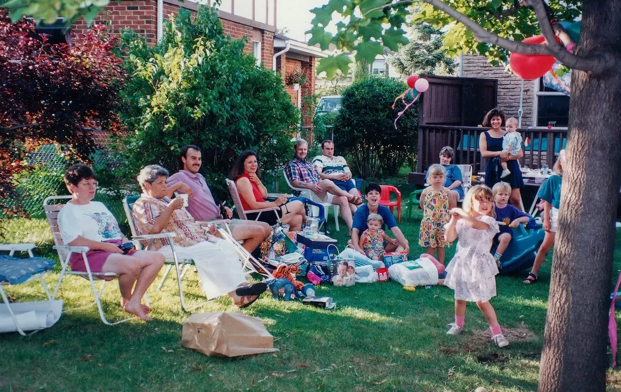 A back garden party across several generations, chairs on the grass and balloons tied up