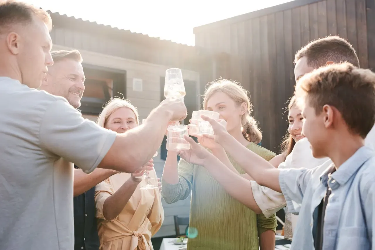 Hands raising glasses in a toast around an outdoor table in low sun